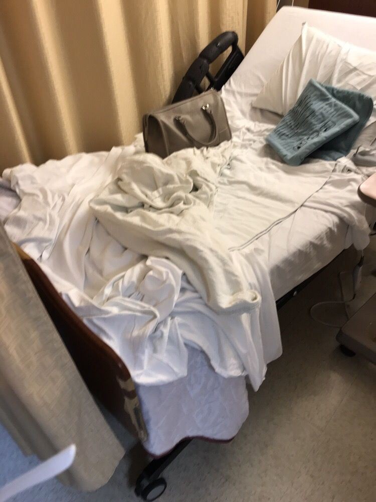 An unmade hospital bed with rumpled sheets and pillows.