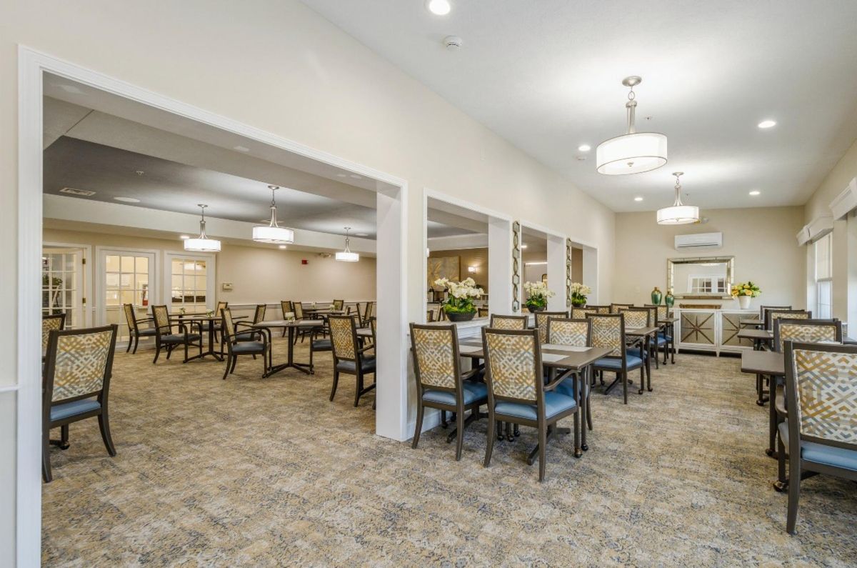 A spacious dining room with neatly arranged tables and chairs under elegant lighting.