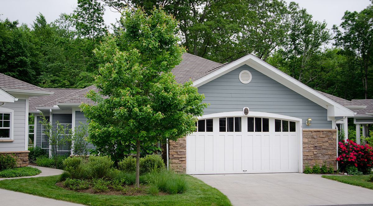 A suburban house with a two-car garage and a tree in the front yard.