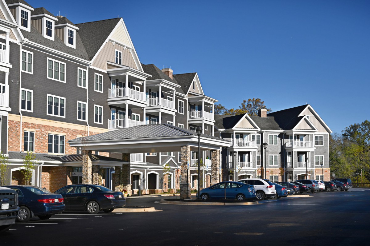 A hotel building with multiple balconies and a parking area on a sunny day.