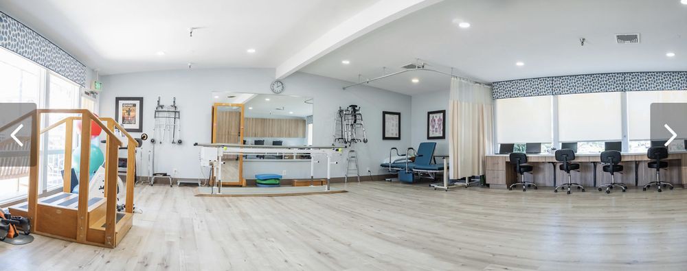 A spacious rehabilitation center equipped with physical therapy apparatus and seating.