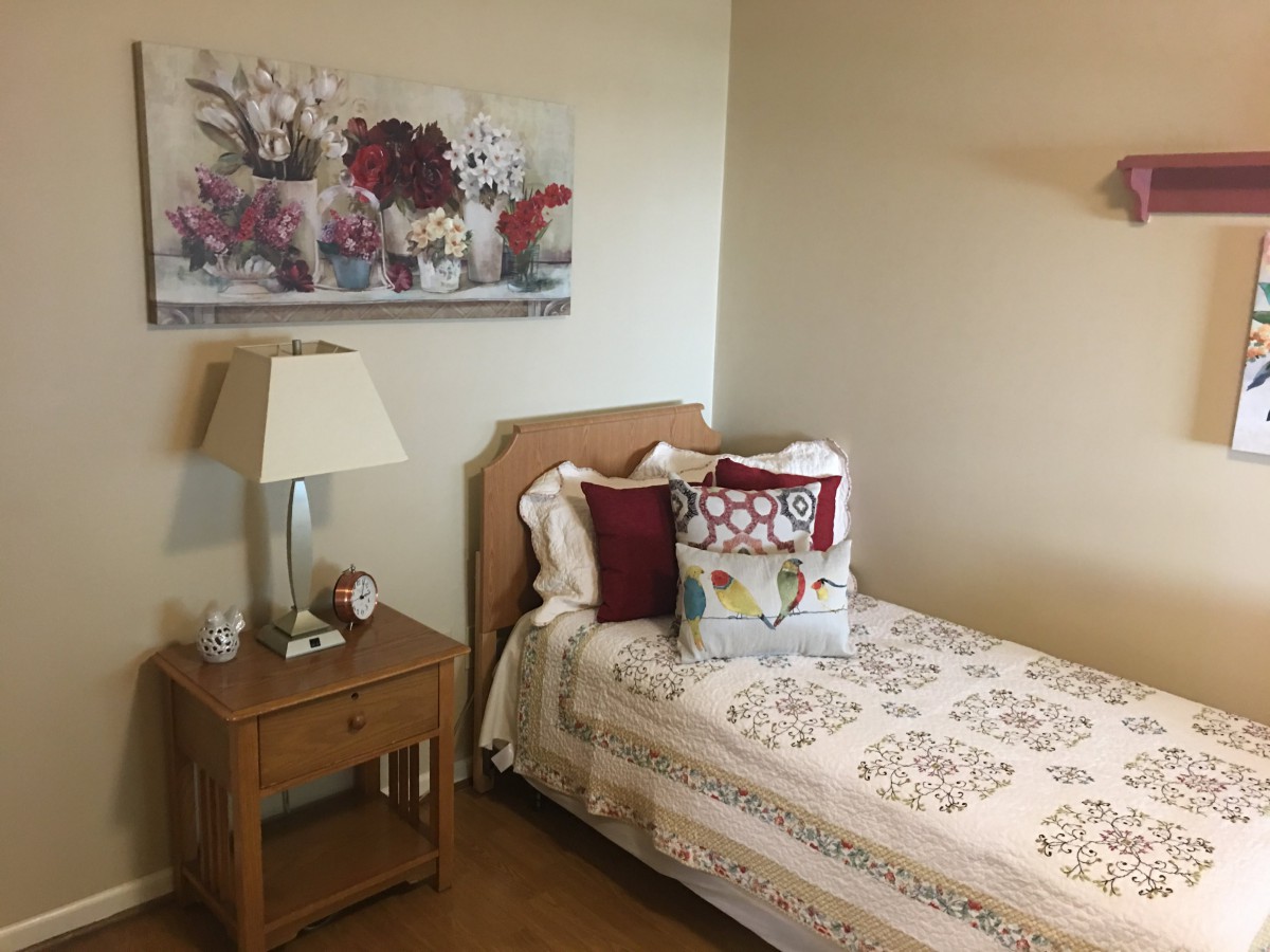 A cozy bedroom with a single bed, nightstand, and floral artwork.