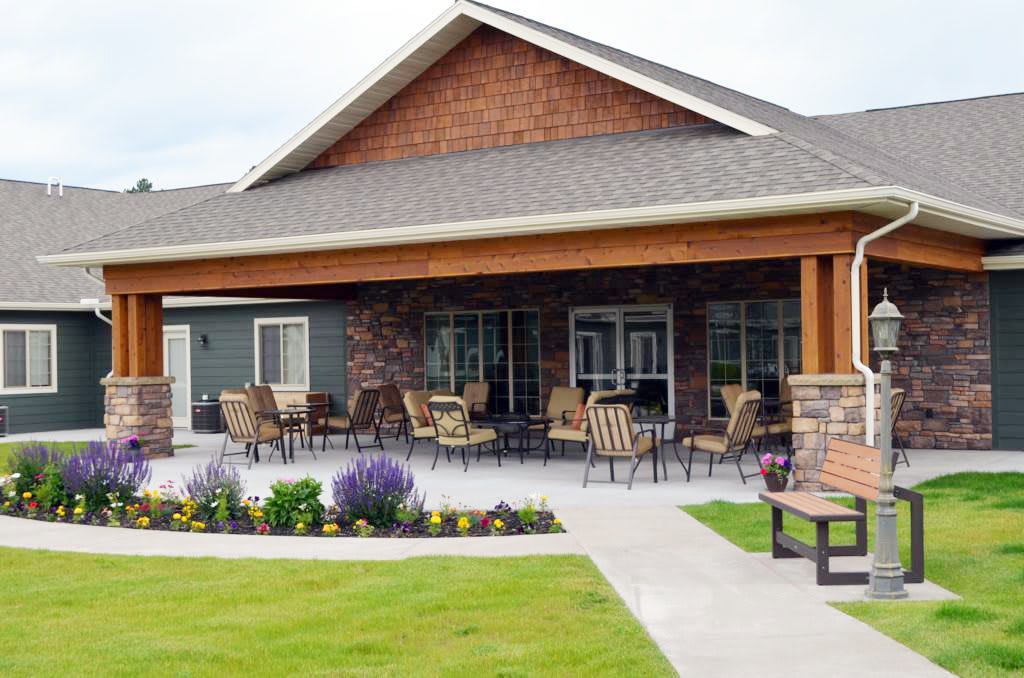 A patio with chairs and tables outside a building, surrounded by landscaping and a well-maintained lawn.