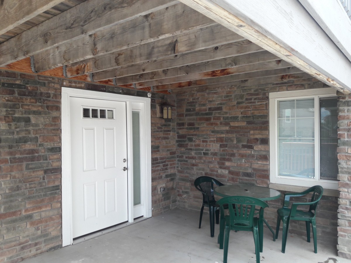 A cozy porch area featuring a stone wall, door, window, and outdoor seating with a table and chairs.