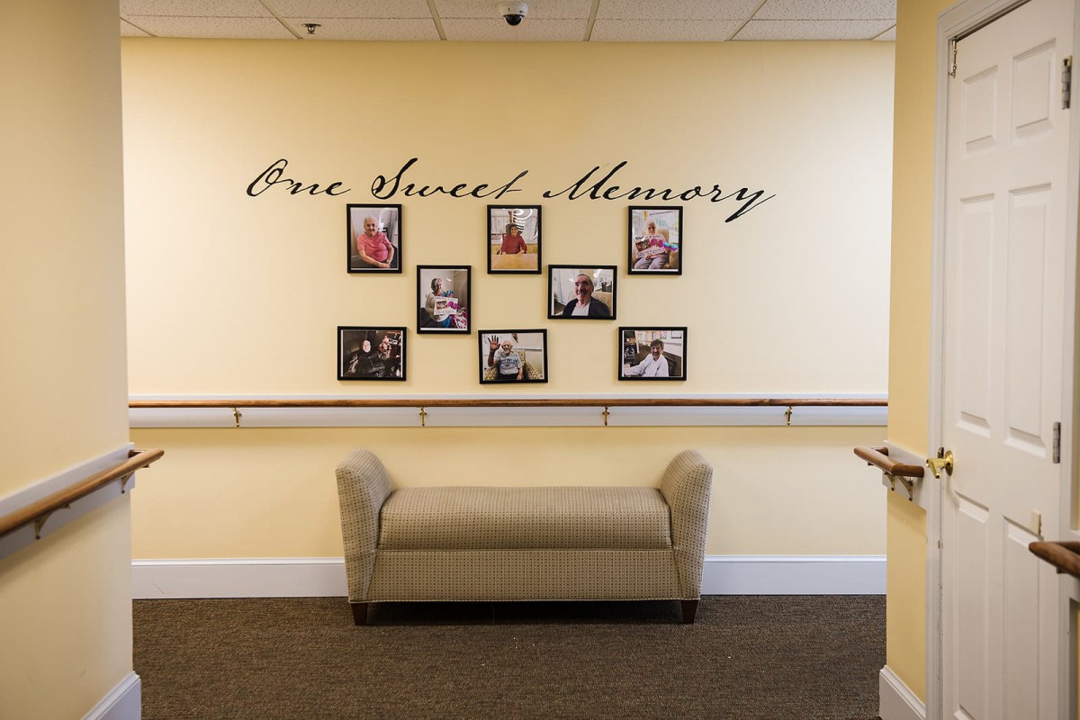 A memory wall with framed photographs and the inscription 'One Sweet Memory' above a comfortable bench.