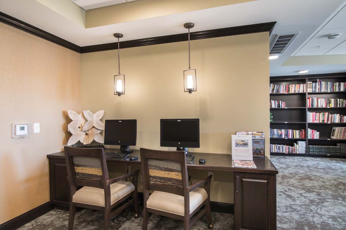 A well-organized office workspace featuring two computers on a shared desk with chairs and pendant lighting.