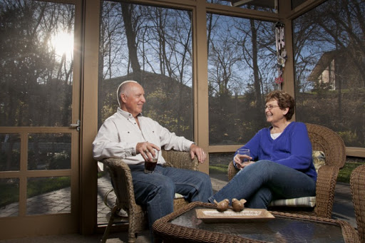 A friendly conversation between two individuals in a cozy indoor setting with a view of the outdoors.