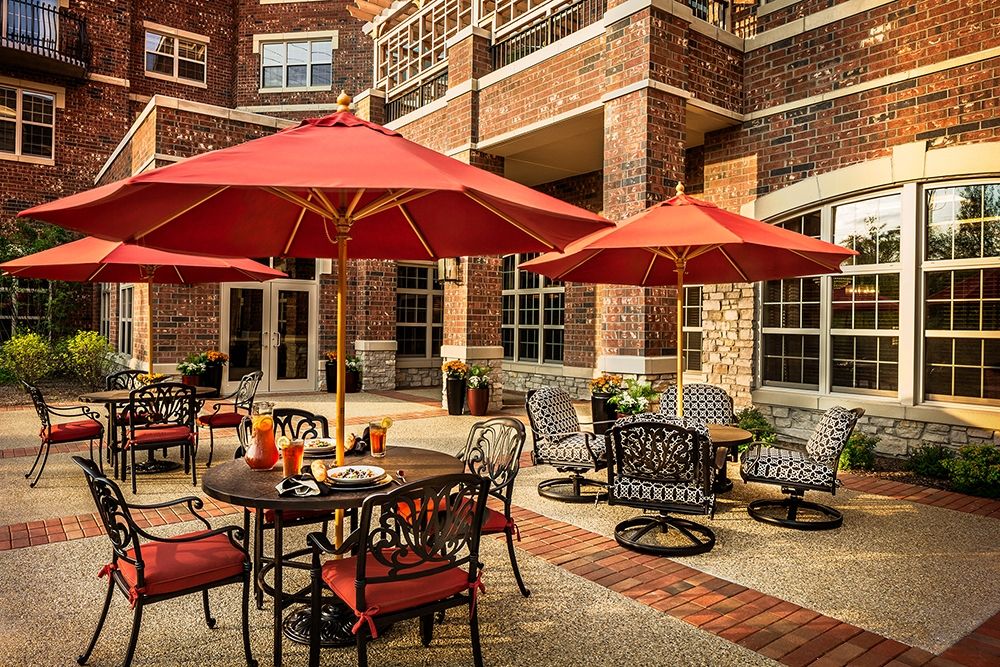 A charming outdoor patio area featuring tables with red umbrellas set against a brick building backdrop.