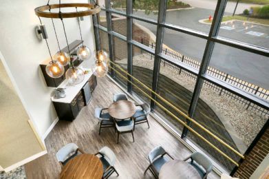 A modern dining area with large windows allowing natural light to flood in, featuring wooden flooring and stylish hanging lights.