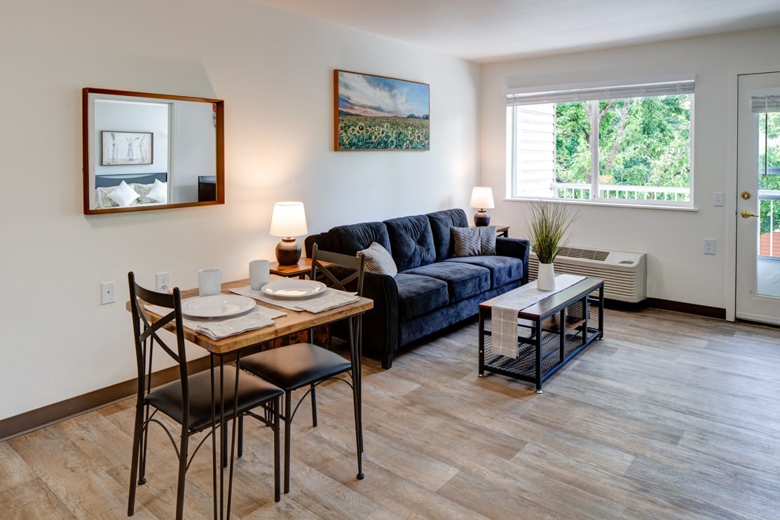 A cozy living room with a sofa, dining set, and natural lighting.