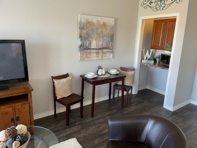 Cozy dining area with a small table and chairs, featuring artwork and an open view into the kitchen.