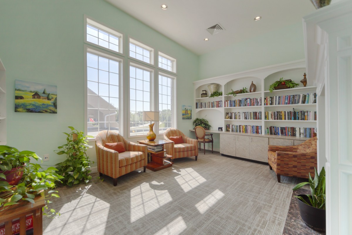 A cozy reading room with large windows, armchairs, and a well-stocked bookshelf.