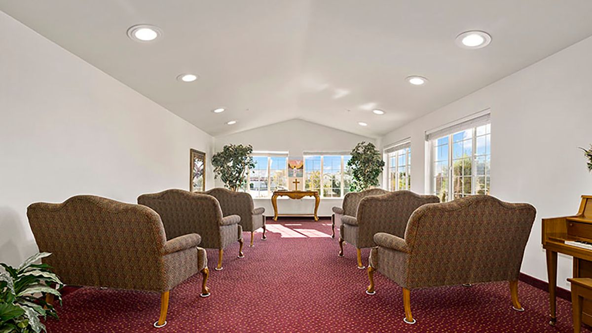 A well-lit waiting room with arranged chairs and a desk, featuring large windows and indoor plants.