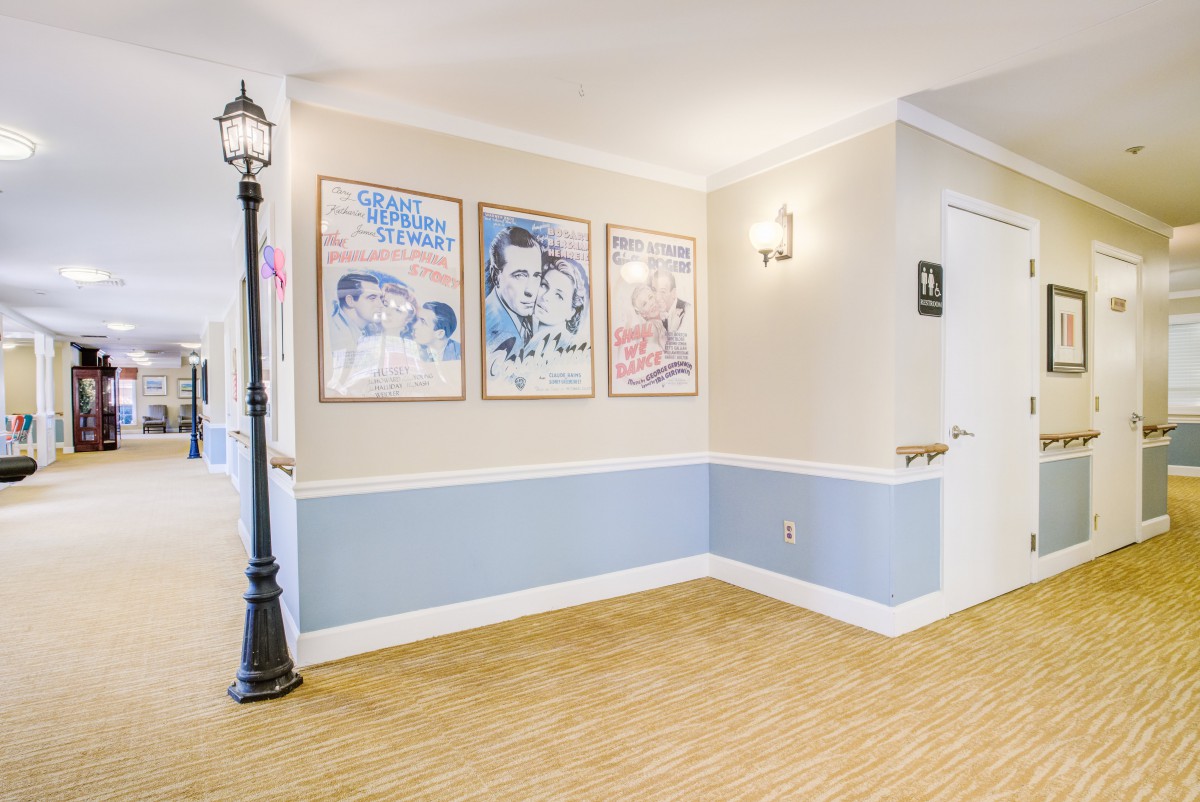 A well-lit hallway featuring vintage posters on a blue and white wall, with a decorative lamppost and modern light fixtures.