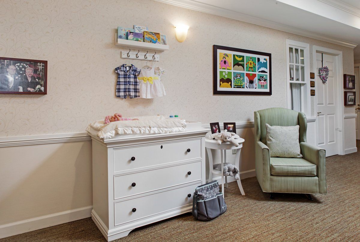 A cozy nursery featuring a white dresser with baby clothes and decor, alongside a comfortable chair, creating a welcoming space for a newborn.