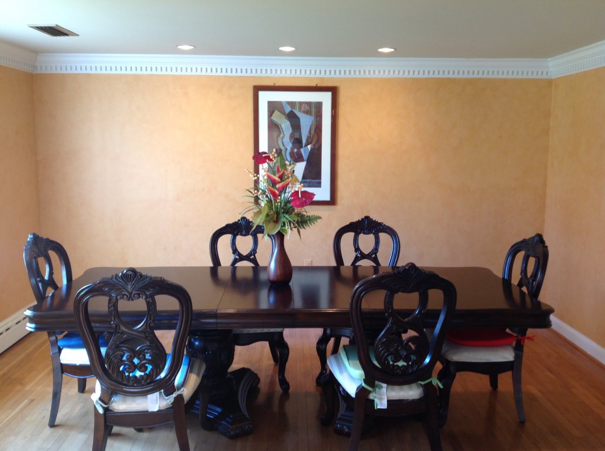 A well-appointed dining room featuring a dark wooden table with six chairs, a vase with flowers at the center, and a painting on the wall.