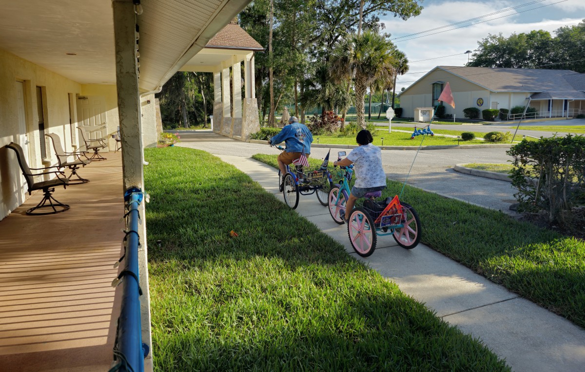 Two people riding bicycles down a sidewalk in a neighborhood setting.