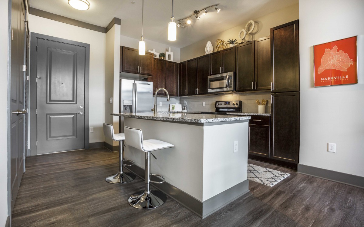 A modern kitchen interior featuring an island with seating, dark cabinets, and stainless steel appliances.