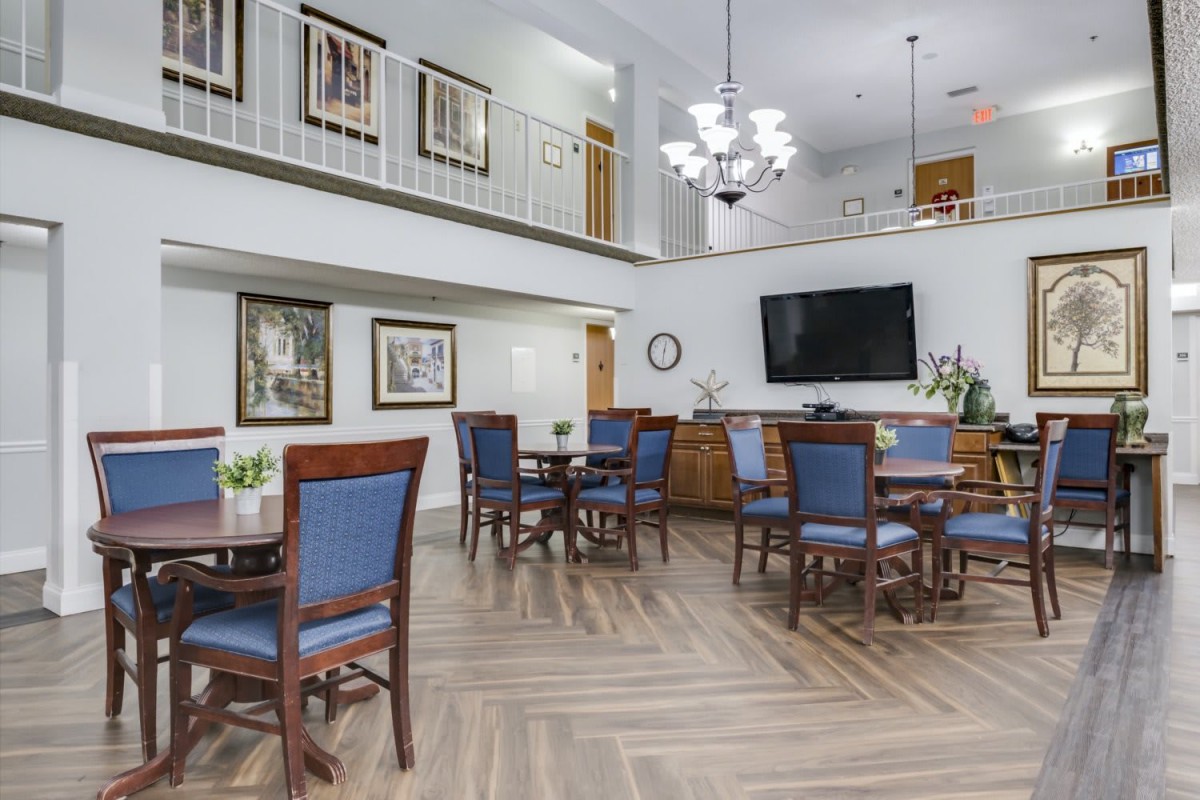 A spacious and elegant dining area featuring wooden tables and chairs, a large chandelier, and a wall-mounted television.
