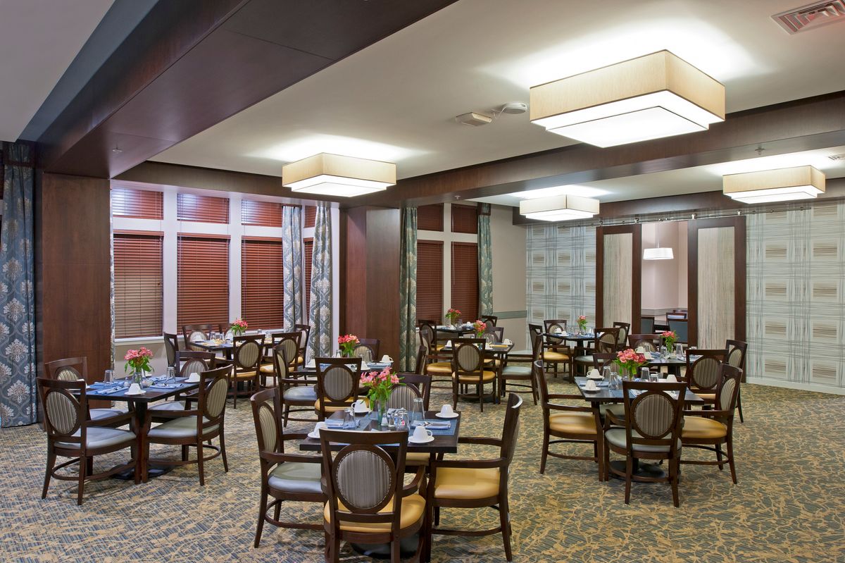 A well-arranged dining area with multiple tables and chairs, featuring elegant lighting and decor.