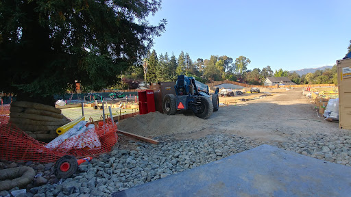 A tractor working on a construction site, surrounded by gravel and equipment under a clear blue sky.