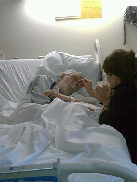 A person visits an elderly patient lying in a hospital bed.