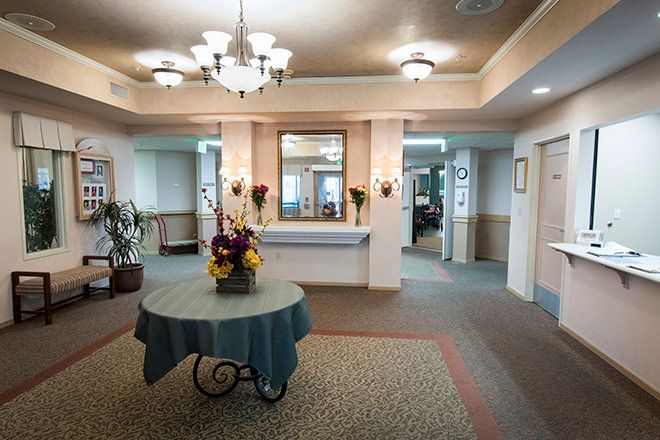 A well-lit lobby with a reception desk, featuring elegant chandeliers and a center table adorned with flowers.