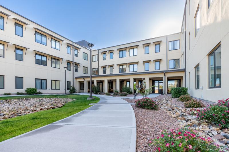 A modern three-story building with a landscaped courtyard and paved pathway.