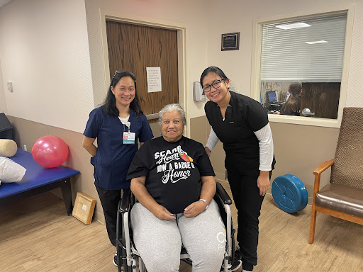 A patient in a wheelchair poses with two healthcare professionals during a rehabilitation session.