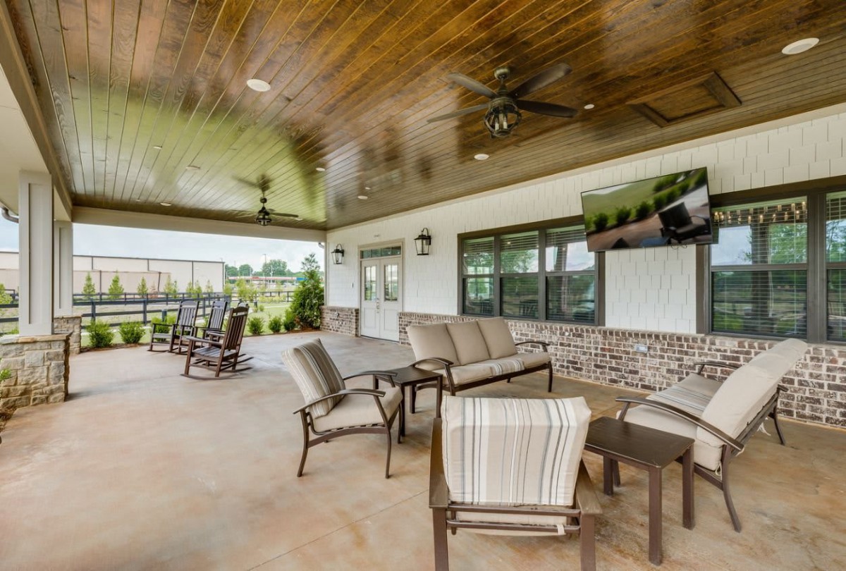 A spacious and modern outdoor patio featuring comfortable seating and a ceiling fan, offering a relaxing garden view.