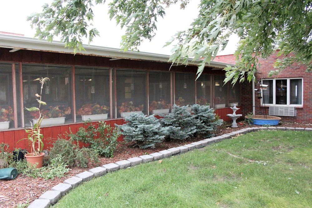 A well-maintained garden with bushes and a lawn in front of a screened porch.