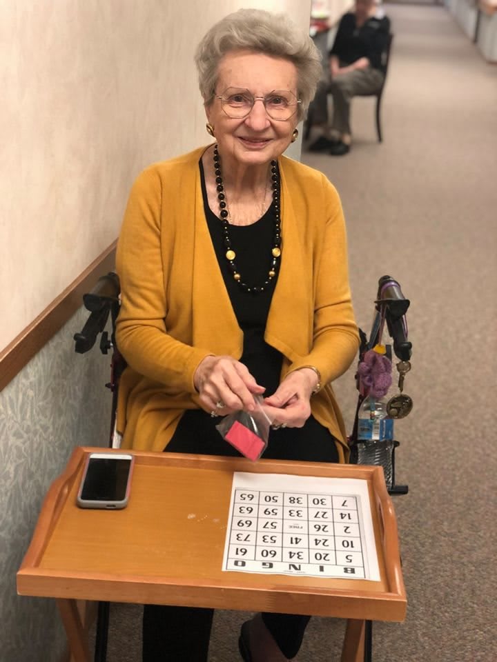 An elderly woman smiling while playing bingo indoors.