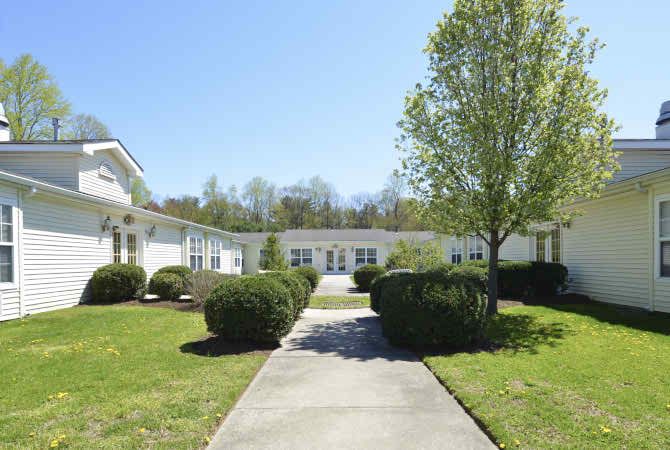 A scenic view of a white building surrounded by trees and bushes under a clear blue sky.
