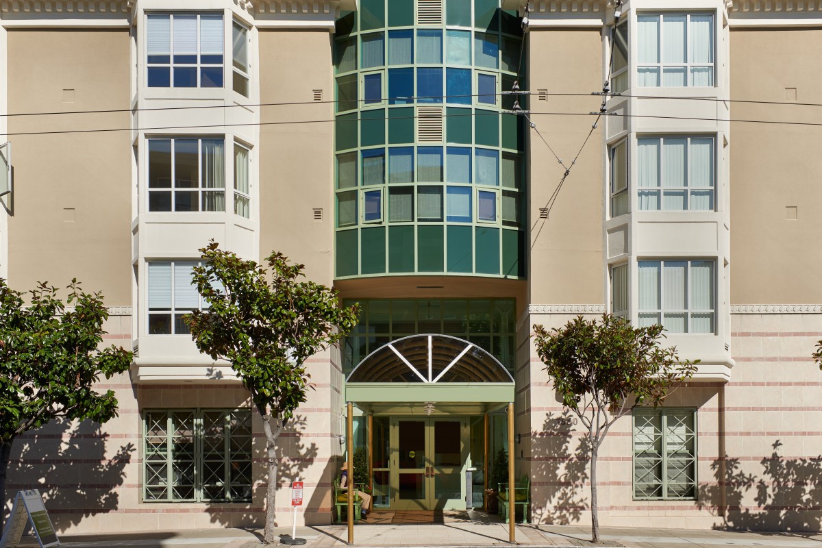 Front view of a modern apartment building with trees lining the entrance.
