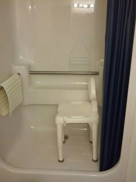 An accessible shower with a chair and handrail.