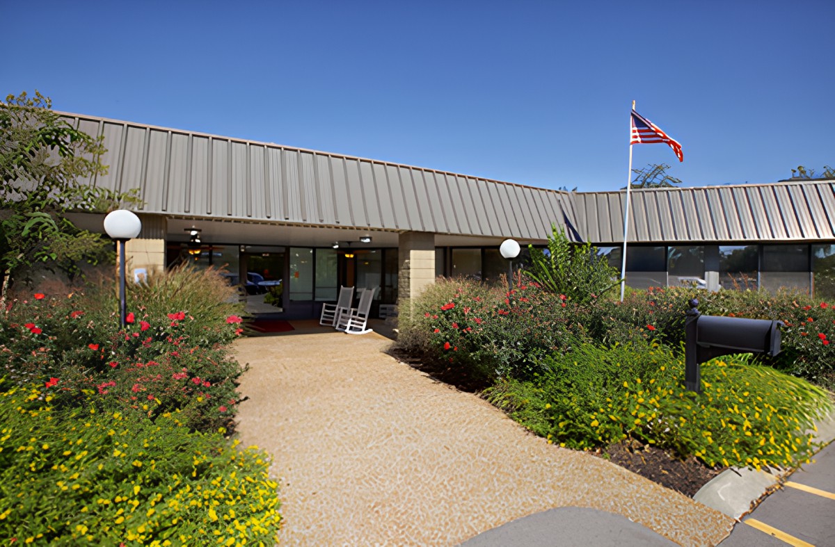 A building entrance with a landscaped garden and flag on a clear day.