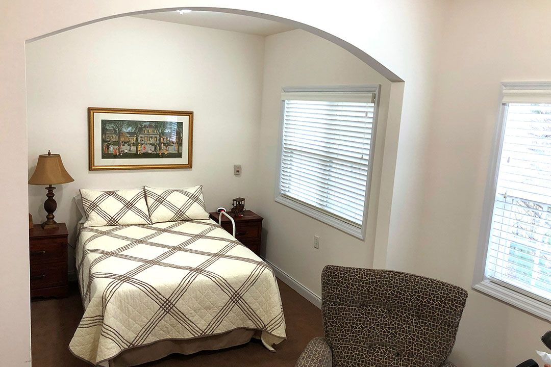 A cozy bedroom with a bed, side table, and a window with blinds.