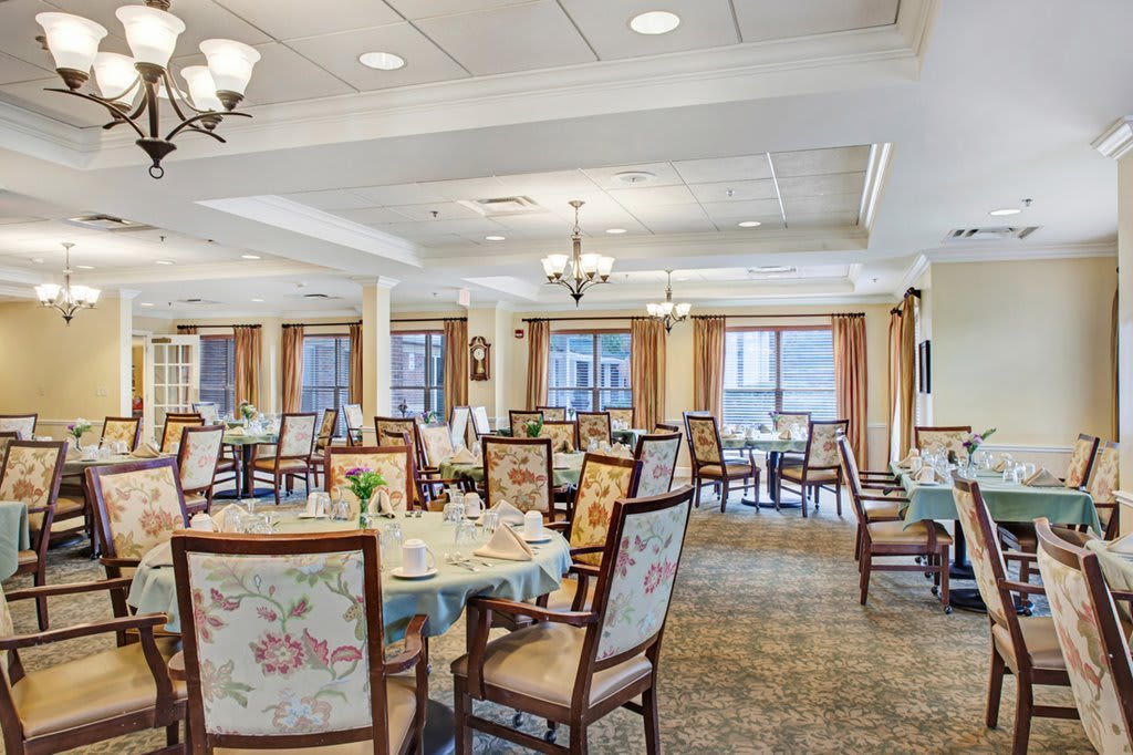 An elegantly designed dining room with neatly arranged tables and chairs, featuring chandeliers and large windows.