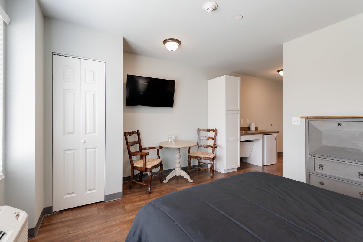 A cozy bedroom with a TV, seating area, and wood flooring.