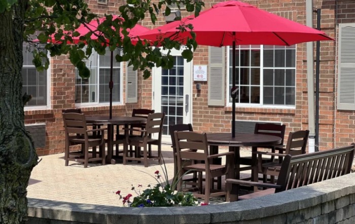 An inviting patio with wooden tables and chairs shaded by red umbrellas outside a brick building.