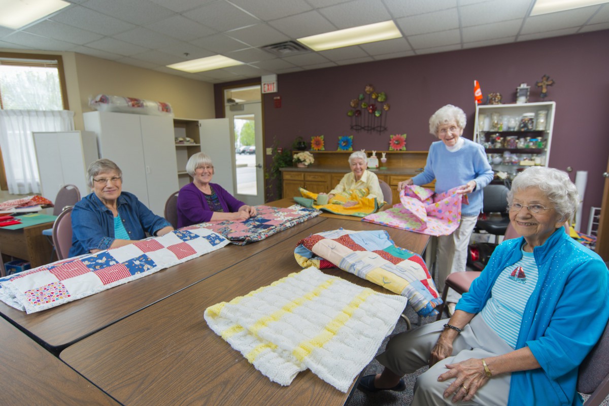 A group of senior citizens enjoy quilting together in a community space.