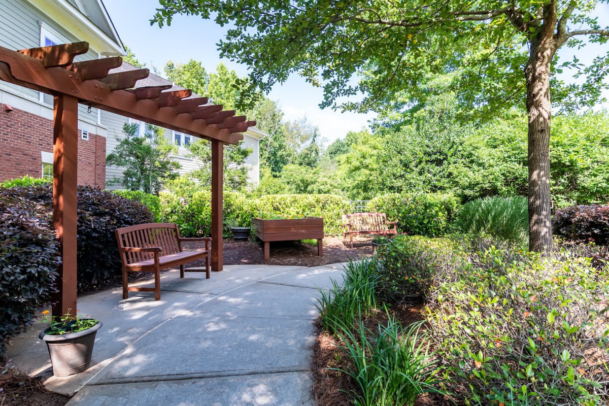 A serene garden patio with a wooden pergola and comfortable benches surrounded by lush greenery.