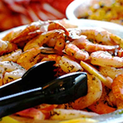 A plate of seasoned cooked shrimp served with tongs at a buffet.