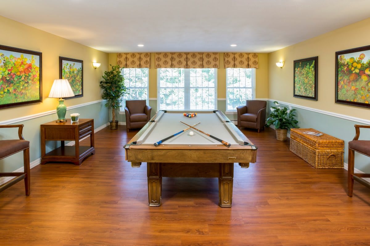 A cozy game room featuring a pool table, comfortable seating, and warm wooden flooring.