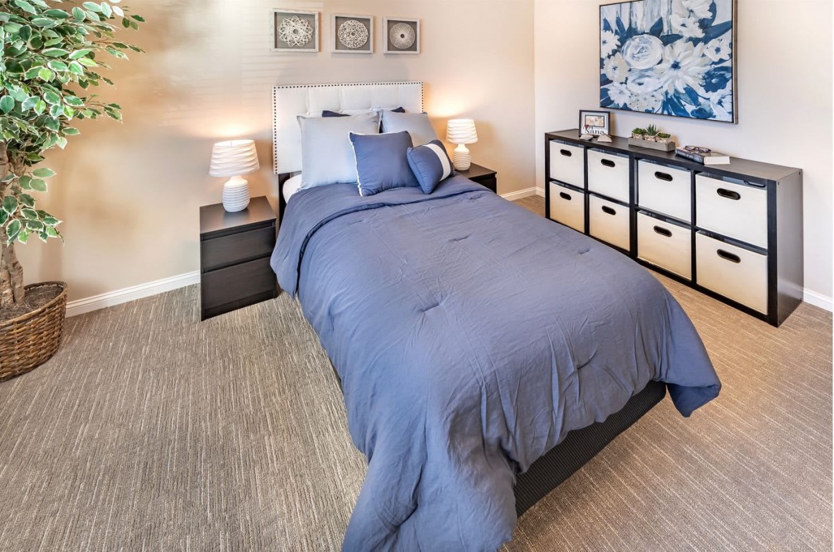 A cozy bedroom with a neatly made bed, bedside lamps, and organized storage.