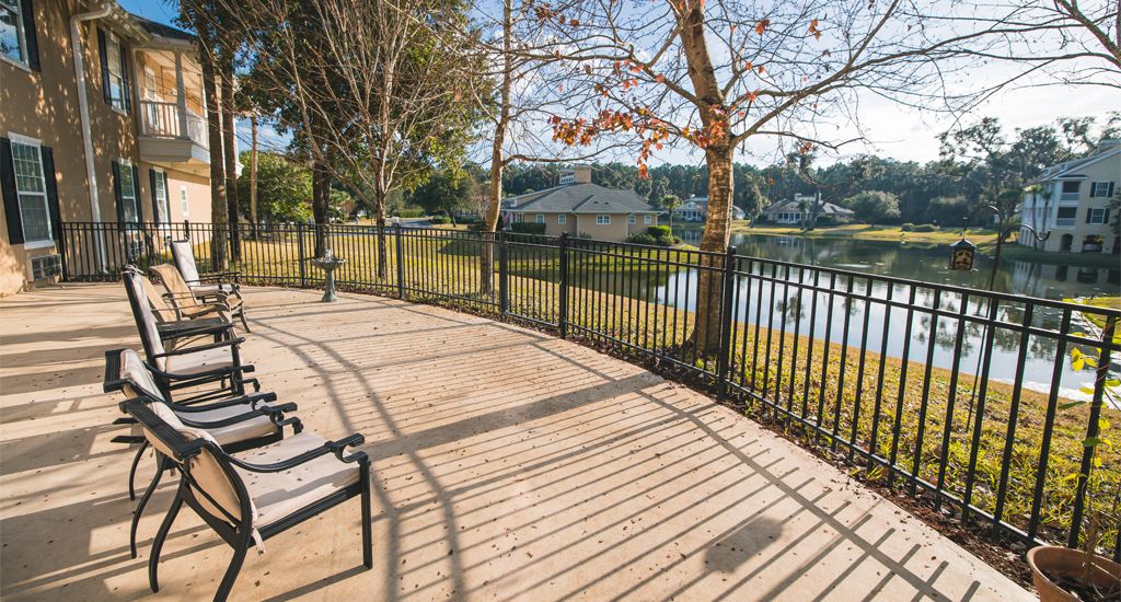 A serene park with benches overlooking a tranquil lake, surrounded by trees and illuminated by sunlight.