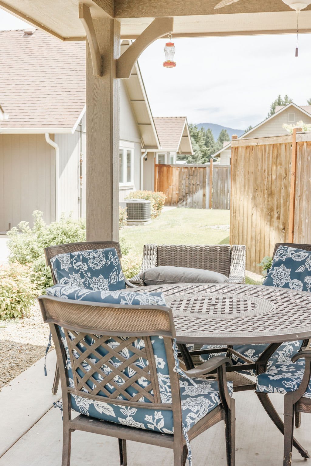 A cozy patio with a round table and chairs, overlooking a backyard enclosed by a wooden fence.