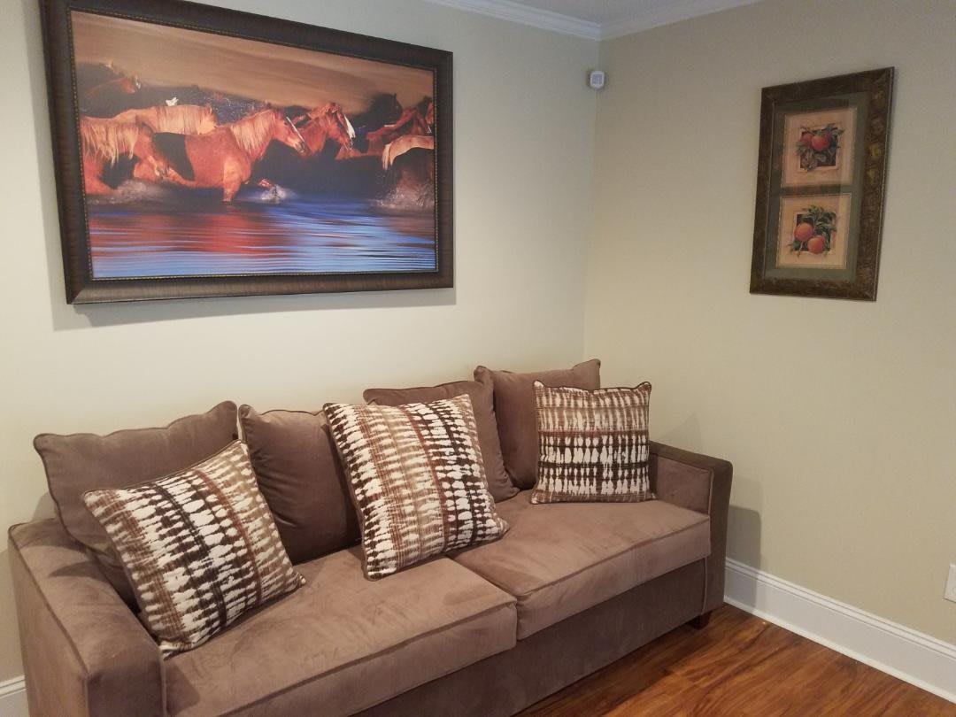 A cozy living room with a brown sofa adorned with patterned cushions, complemented by wall art and framed pictures.