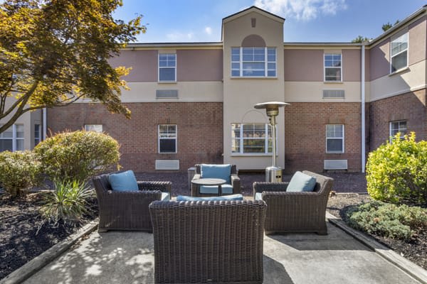 A cozy patio seating area with wicker furniture in front of a two-story building.