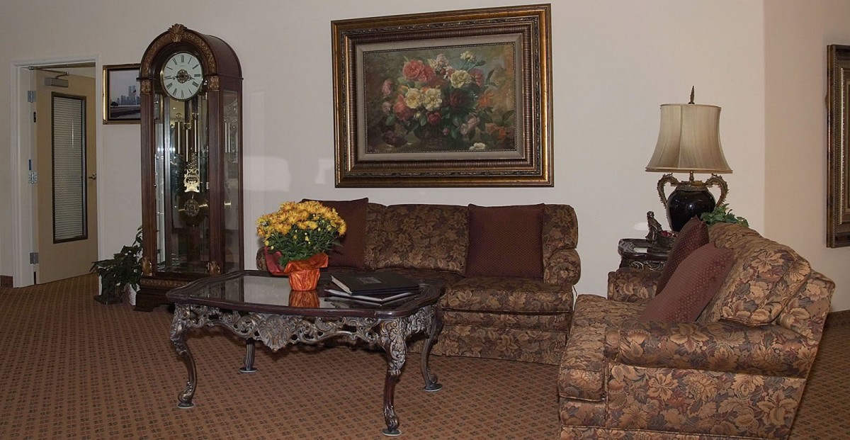 A traditional living room with a patterned sofa, ornate coffee table, and a floral arrangement under an elegant framed painting.